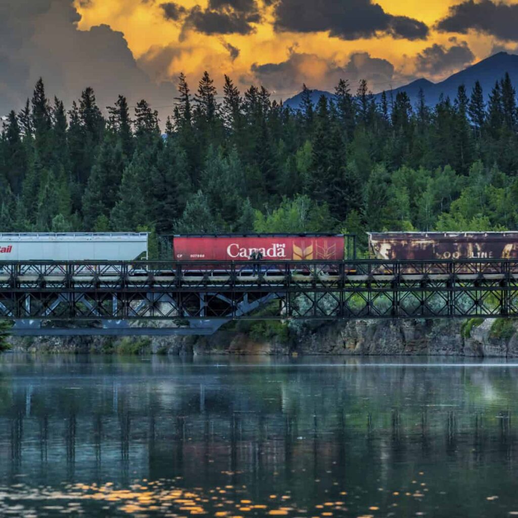 Canadian National Railway vs. Canadian Pacific Kansas City: Which Railroad Stock Is a Better Buy in 2026? Train cars pass over trestle bridge in the mountains